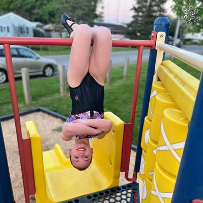 Gymnast hanging on playground in gymnastics leotard.