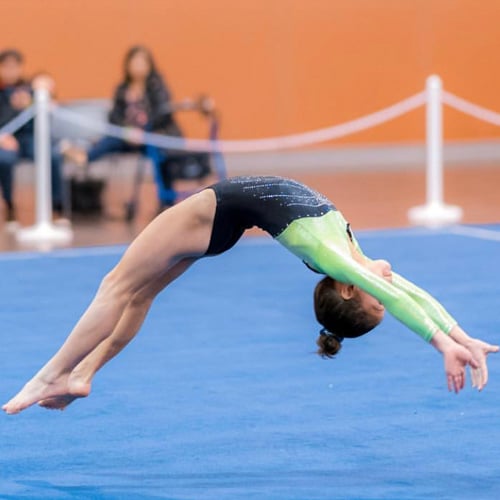 A gymnast doing a back handspring in a green and black leotard.