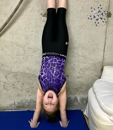 Gymnast doing a handstand in a purple gymnastics leotard.
