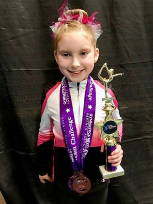 Gymnast with medals and trophy at a gymnastics meet.