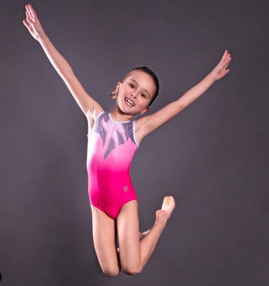 Gymnast jumping in the air in a pink gymnastics leotard.