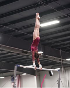 gymnast in burgundy leotard doing giants on bars