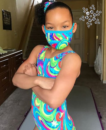 Gymnast in matching rainbow leotard and face mask.